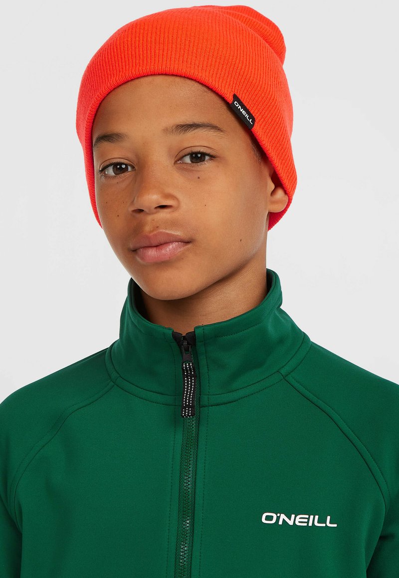 Berretto a righe arancione indossato con una giacca verde con zip dotata di un alto colletto e logo bianco sul lato sinistro del petto. Sfondo bianco puro.