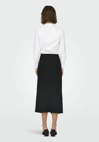 Zwarte midi-jurk met streepjes in een recht model, gecombineerd met een witte met kraag. Heeft een split aan de achterkant en een minimalistisch design.