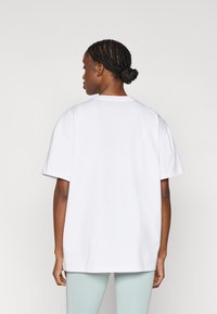 T-shirt surdimensionné en coton blanc à manches courtes et col rond, vu de dos. Texture lisse, sans motifs ni accents visibles.