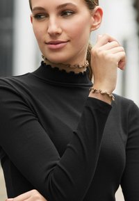 Must mustärjane nööriga turtleneck, millel on laineline, kontrastne pruun krae ja randme detail, pikad sobivad varrukad.
