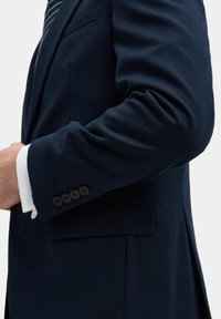 Marineblauwe blazer met gestructureerde schouders, vier zwarte knopen op de manchetten en een enkele borstzak, gemaakt van gladde stof.