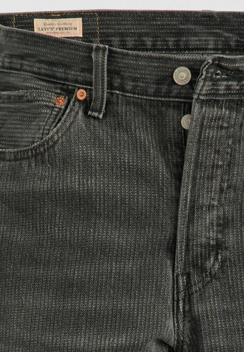 Jeans de mezclilla negra con un acabado texturizado, que cuentan con una cintura reforzada, botón de cobre y una etiqueta que dice "Levi's Premium."