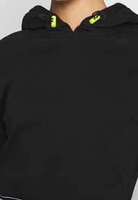 Svart hoodie med en strukturerad tyg, som har en huva med dragsnodd och neongula stoppare samt en kort, croppad längd.
