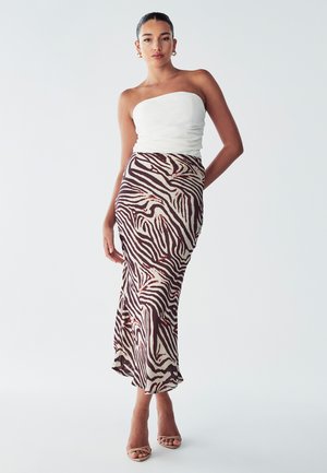 Top bez naramenica u bijeloj boji uparen s midi suknjom u smeškastom i krem uzorku zebra, koja ima lepršavi dizajn i suptilni sjaj. Elegantne nude potpetice.