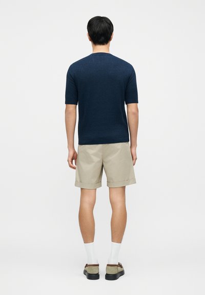 Pull côtelé marine à manches courtes, associé à un short beige plié, des chaussettes blanches et des chaussures grises, vu de dos.