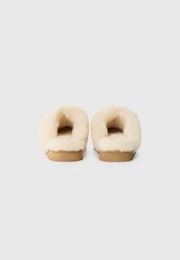 Kremfargede tøfler med myk, fluffy innside, åpen bakdesign og sandfarget såle. Enkle, koselige konstruksjoner uten dekorasjoner.
