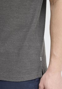 Gray knit t-shirt with short sleeves, featuring a side split at the hem and a small fabric label. Smooth texture and fitted design.