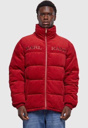 Rød corduroy pufferjakke med høj krave, der har quiltede sektioner og broderet "KARL KANI" branding på forsiden. Lynlåslukning.
