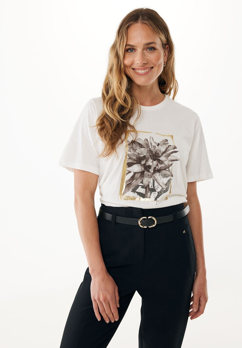 Bílá tričko s černým květinovým potiskem orámovaným zlatým okrajem, spárované s černými kalhotami s vysokým pasem a černým opaskem se zlatou sponou.