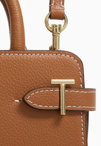 Sac à main en cuir marron avec une surface texturée, des accents dorés, des coutures blanches et un accent en forme de T sur le rabat de fermeture.