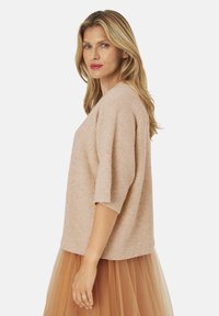 Lys pink sweater med struktureret strik, korte ærmer og afslappet pasform, parret med en gennemsigtig brun tylskørt.