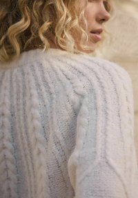 Maglione chunky a trecce in lavorazione cable-knit, caratterizzato da trecce sollevate e anelli testurizzati, con filato morbido e soffice che crea profondità e calore.