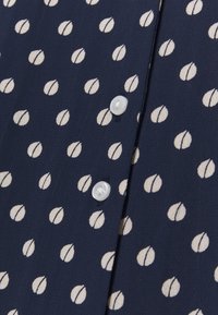 Marinblus med ett vitt abstrakt prickmönster, med knappstängning fram och en lätt, slät tygkvalitet.