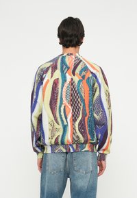 Mønstret striktrøje i mange farver med en løs pasform, der har abstrakte bølgemønstre i livlige nuancer og ribbede manchetter. Båret over denimjeans.