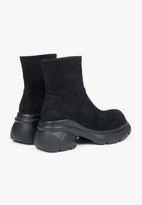 Black suede ankle boots with a chunky black rubber sole, featuring a smooth texture and a rounded design. Stitched upper detailing.