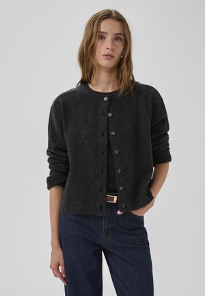 Mørkegrå uldcardigan med rund halsudskæring, knaplukning og let oversized pasform; kombineret med mørke denimjeans.