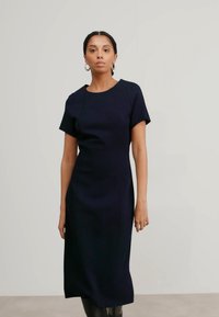 Námornícky modré priliehavé šaty s krátkymi rukávmi, okrúhlym výstrihom a štrukturovanými švami. Hladká látka, dĺžka po kolená a minimalistic design.