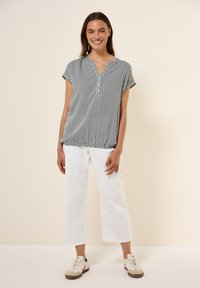 Camicetta a righe bianche e nere a maniche corte con bottoni, abbinata a pantaloni bianchi alla caviglia e sneakers beige. Tessuto dalla superficie liscia.