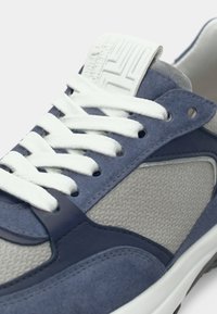 Αθλητικό παπούτσι από γαλάζιο σουέτ και δίχτυ με λευκά κορδόνια και υφή στη γλώσσα. Διαθέτει σκούρες μπλε λεπτομέρειες και διακριτικές ραφές.