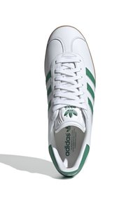 Valkoiset Adidas-lenkkarit, joissa on vihreät kolme raitaa, sileä nahkapinta, reikäkuvioitu kärki ja kumiulkopohja. Logo näkyy kielen ja pohjallisen päällä.