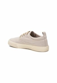Zapatilla de lona beige con punta redondeada, cordones beige y suela de goma texturizada. Parte superior lisa con una pestaña en el talón para facilitar el uso.