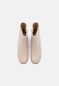 Pár béžových kotníkových bot s bočními zipy a čtveratými špičkami, zobrazené zvrchu na bílém pozadí.