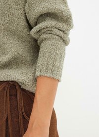 Maglione grigio con texture, dalla vestibilità morbida e bordi arrotolati, abbinato a una gonna marrone con texture e un dettaglio in vita legato.