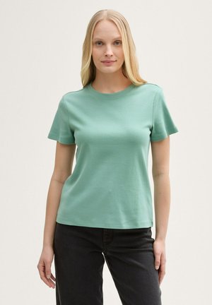 T-shirt vert menthe à manches courtes avec un col rond, fabriquée en coton doux, présentant une coupe décontractée et une texture lisse. Associée à un jean noir.