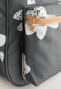 Grå tote-väska prydd med vita blommönster och svarta prickar. Dragkedja med en stjärnformad dragtab; texturerad tygdetalj.
