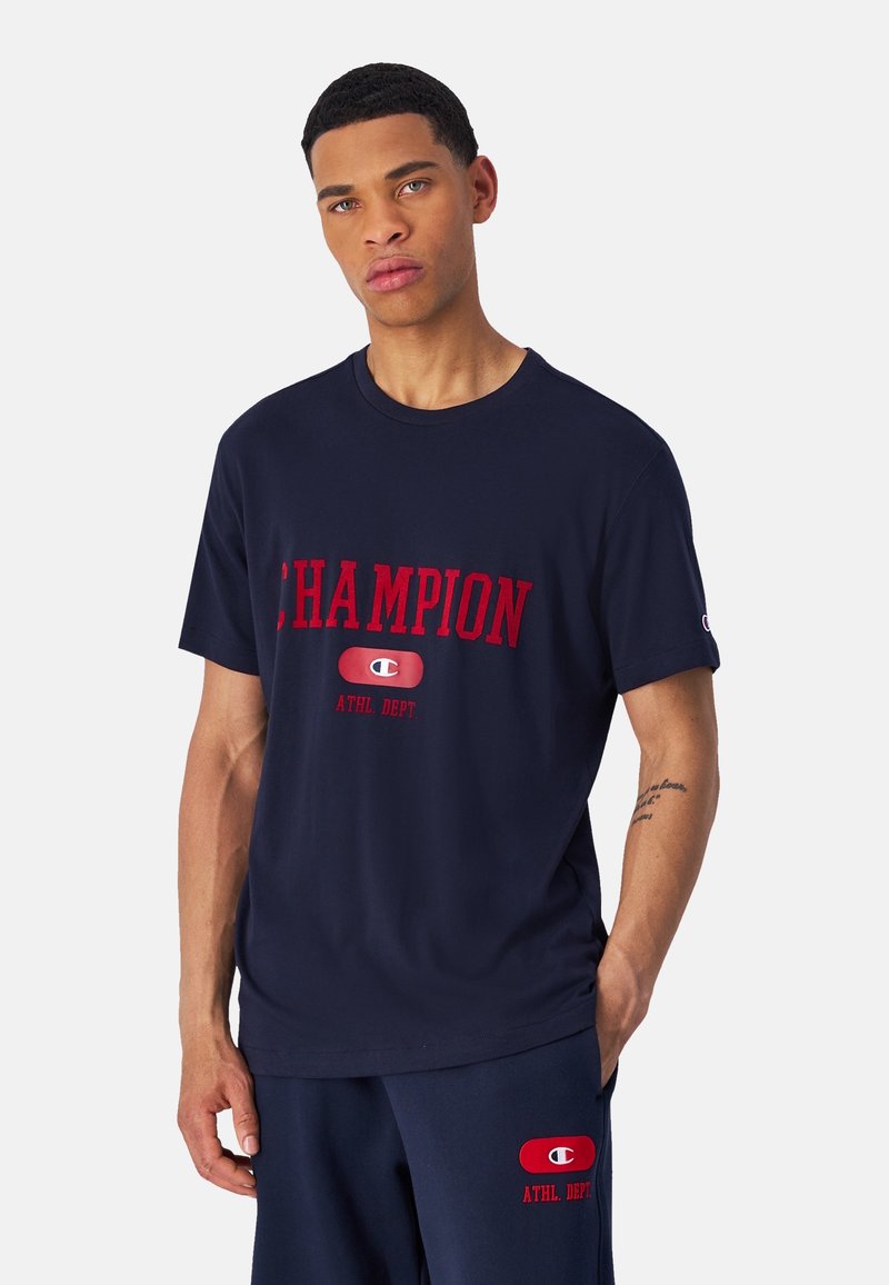 Navyblauwe katoenen T-shirt met een rode "CHAMPION" logo. Ronde hals met korte mouwen. Horizontale tekstprint en logo-accenten.
