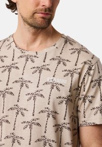 Beige t-shirt made of cotton featuring a brown palm tree pattern, with "SEASIDE" text in white on the chest area.