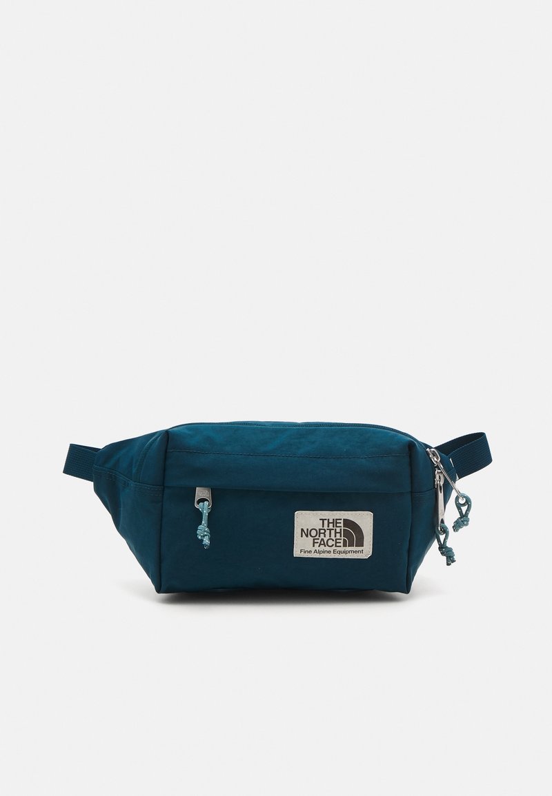 Sac banane bleu sarcelle foncé avec poche avant zippée, sangle réglable et écusson logo "The North Face Fine Alpine Equipment".