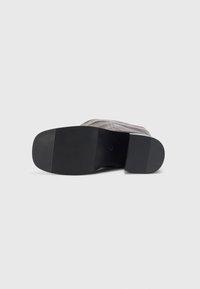 Semelle de chaussure grise avec une surface en caoutchouc noir texturé et des stries subtiles. Le côté latéral présente des coutures et un dessus en tissu lisse.