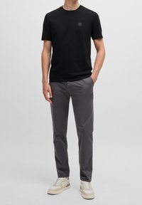 Svart bomullströja med rund hals och liten logotyp, i kombination med grå chinos och beige sneakers. Enkelt, avslappnat outfit.