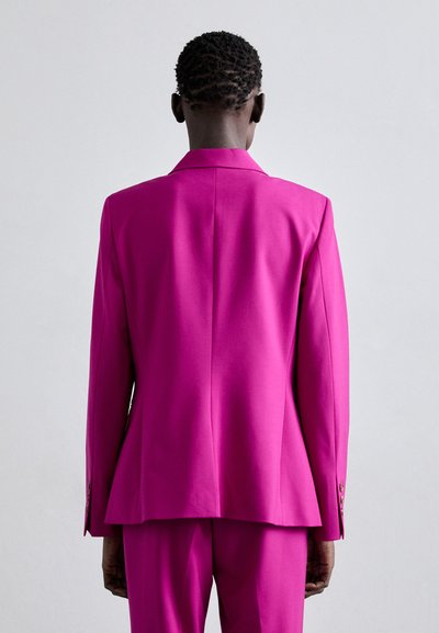 Kohandatud roosa bleiser, millel on nurgeline krae, ühekordne seljatuul ja kahe nööbiga mansetid, valmistatud siledast ja struktureeritud kangast.