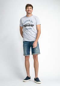 T-shirt en coton gris avec un graphique de voiture noire et du texte bleu, associé à un short en denim usé. Le short est retroussé au niveau de l'ourlet.