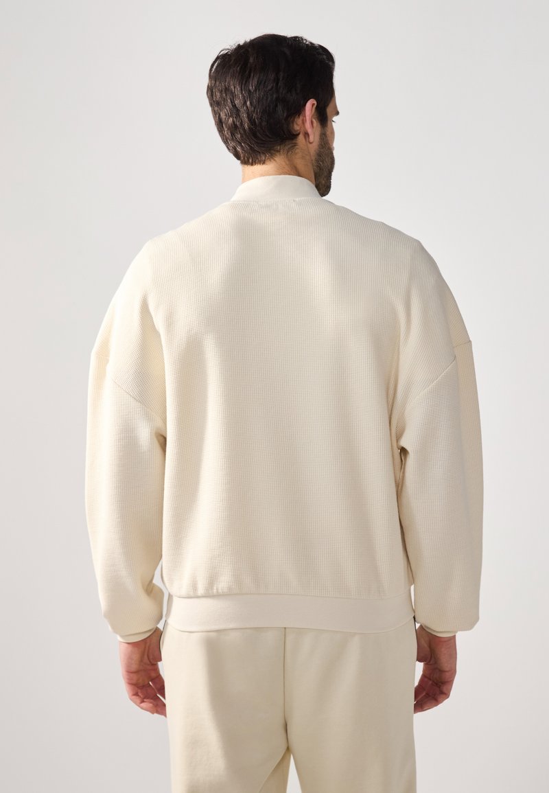 Beige Sweatshirt mit strukturierter Textur, geripptem Muster, weiten Ärmeln und lockerer Passform. Mit Rundhalsausschnitt und elastischem Saum. Dezente tonale Akzente.