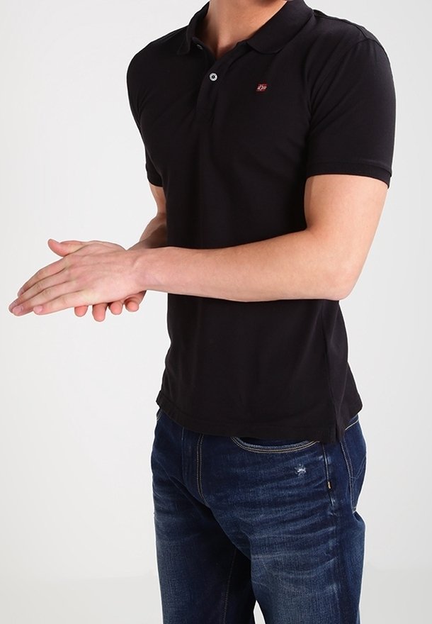 Svart polo skjorta med en liten logotyp på bröstet, i kombination med blå denimjeans. Skjortan har korta ärmar och en klassisk krage.
