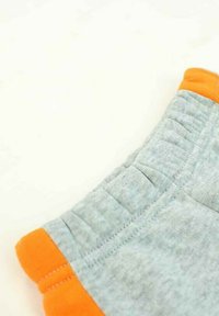 Shorts en tissu gris avec une bordure orange au niveau de la taille ; comportent des coutures visibles et une texture douce, mettant en valeur un design sportif.
