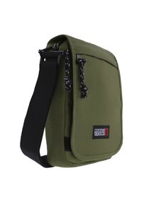 Bolso de hombro de lona verde con una correa ajustable negra, cierre de cremallera y parche con logotipo. Presenta acentos negros y tela texturizada.