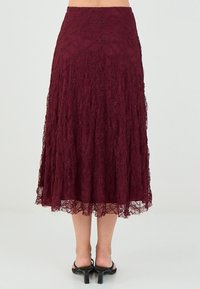 Jupe en dentelle bordeaux avec une coupe évasée, ornée de motifs floraux complexes et d'un ourlet festonné. Taille ajustable.