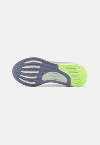 Semelle d'une chaussure de sport avec des motifs de bande de roulement gris et vert néon sur fond blanc, conçue pour l'adhérence et la flexibilité.