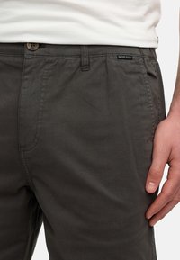 Pantalones de algodón gris oscuro con una textura suave, que presentan un cierre de botón, bolsillos laterales y una etiqueta en la cinturilla que muestra "INDICODE."