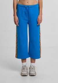 Modré zkrácené tepláky s elastickým pasem, vybavené stahovací šňůrkou a bočními pruhy v červených, žlutých a oranžových vlnách. Měkká textura.