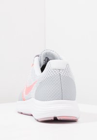 Achteraanzicht van een grijs en witte sportschoen met een roze Nike swoosh op een witte ondergrond en achtergrond.