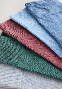 Öt különböző textúrájú kötött anyagminta piros, zöld, kék és szürke színekben, amelyek különböző árnyalatokat és bordázott mintázatot mutatnak a részletgazdagság érdekében.