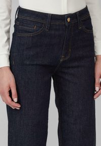 Donkerblauwe denim jeans met een rechte snit, oranje stiksels en een klassiek vijf-pocket ontwerp met metalen hardware bij de tailleband.