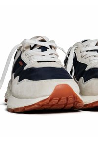 Baskets bleu marine et crème en matériaux en daim texturé et en nylon. Lacets blancs, logo orange, et semelle en caoutchouc avec des motifs de traction.