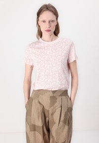 Light pink short-sleeve t-shirt with a floral outline pattern. Relaxed fit. Brown patterned high-waisted pants with side pockets.