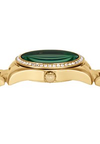 Montre dorée avec un cadran ovale vert, entouré d'une rangée de cristaux transparents. Présente une couronne et un bracelet en maillons.